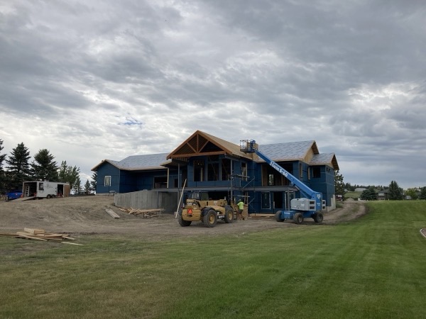 Custom home under construction with timber frame gable and crane on site