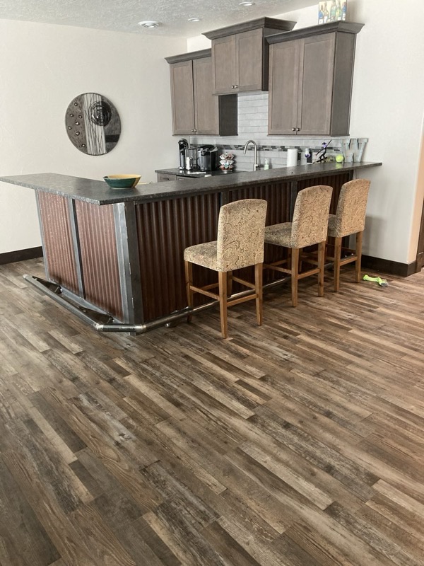 Basement bar with corrugated metal front, concrete countertop, and rustic flooring
